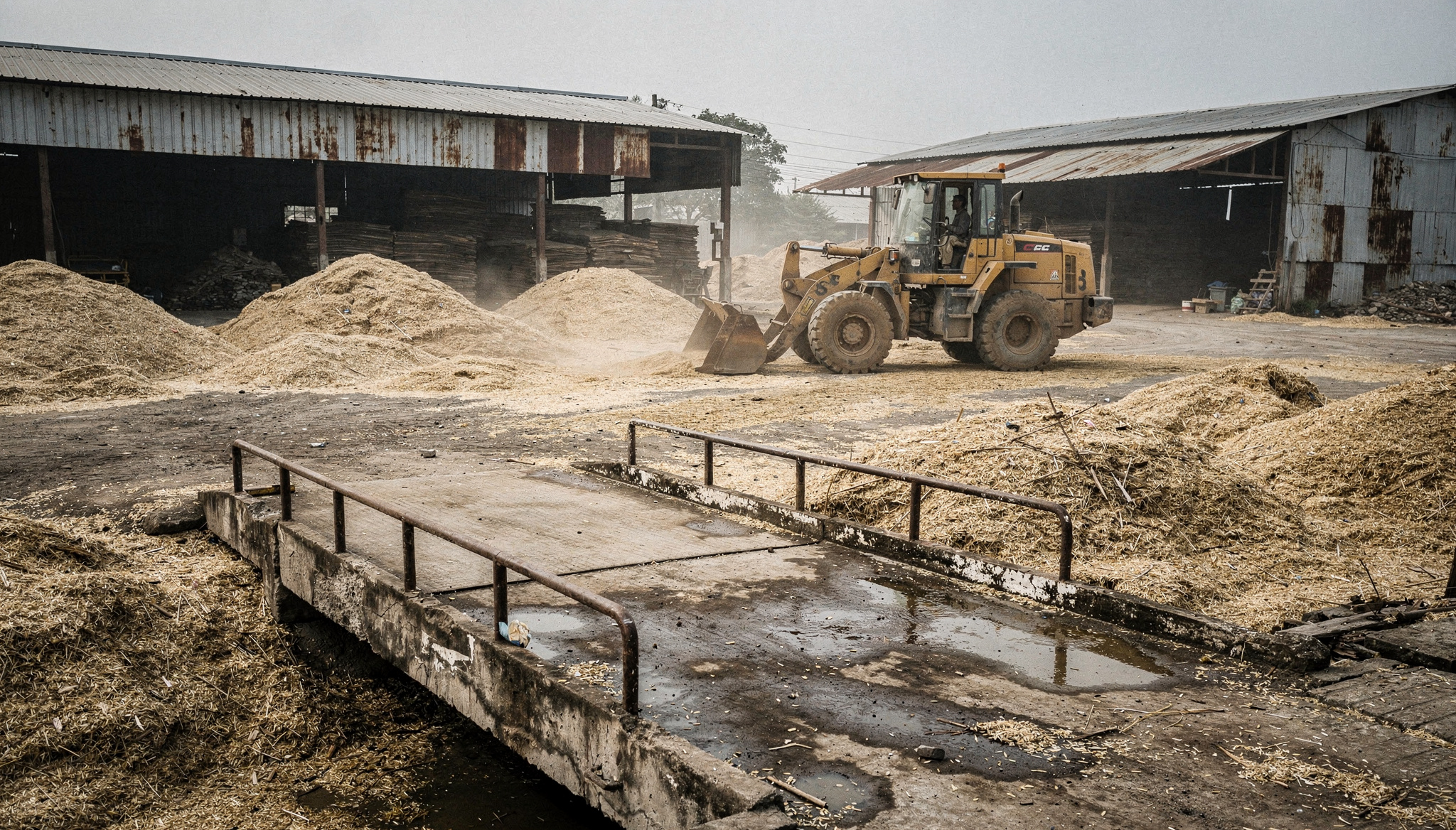 Overcast mill yard with a loader moving rice husk and wood chips
